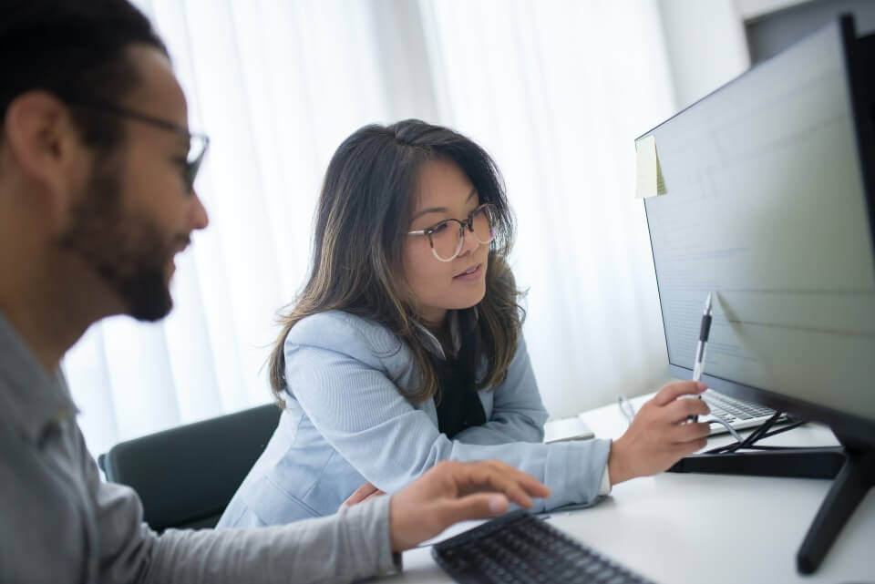 Two co-workers review information on a computer monitor